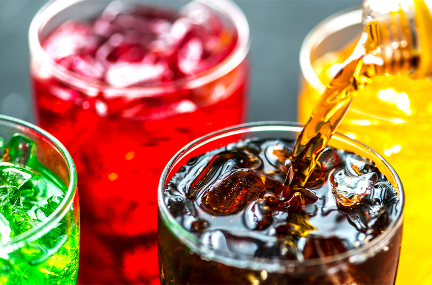 Colorful drinks with ice in assorted glasses, including green, red, brown, and orange beverages on a table (close-up)